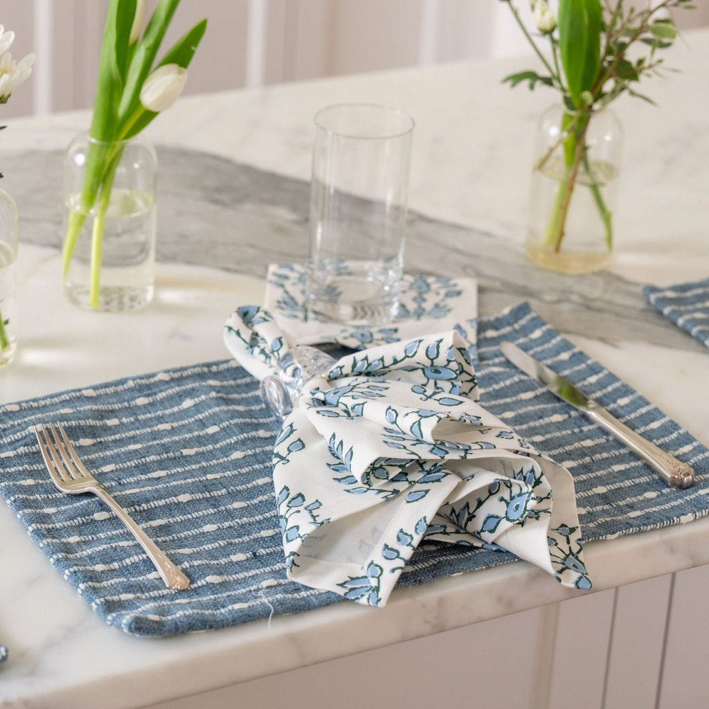 blue patterned napkins on top of dark blue and white striped embroidered placemats for a coastal tablesetting